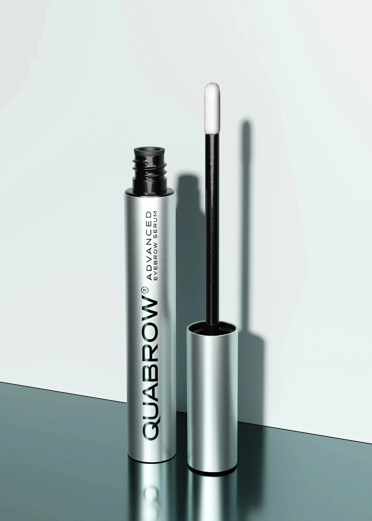 QUABROW Advanced Eyebrow Serum standing upright with the applicator opened on a reflective surface
