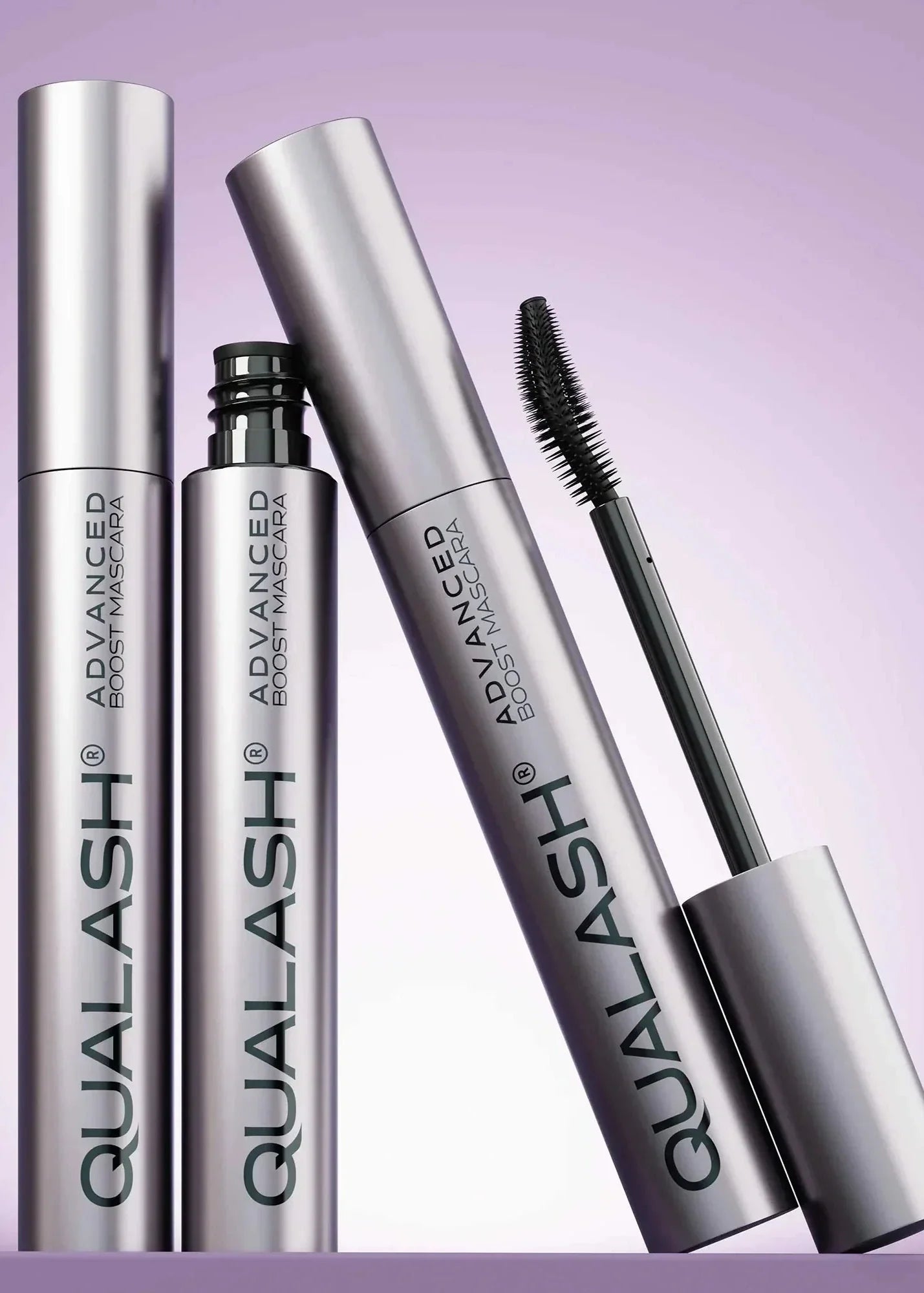 Multiple QUALASH Curl & Lift mascaras arranged creatively on soft purple background with focus on brush and tube