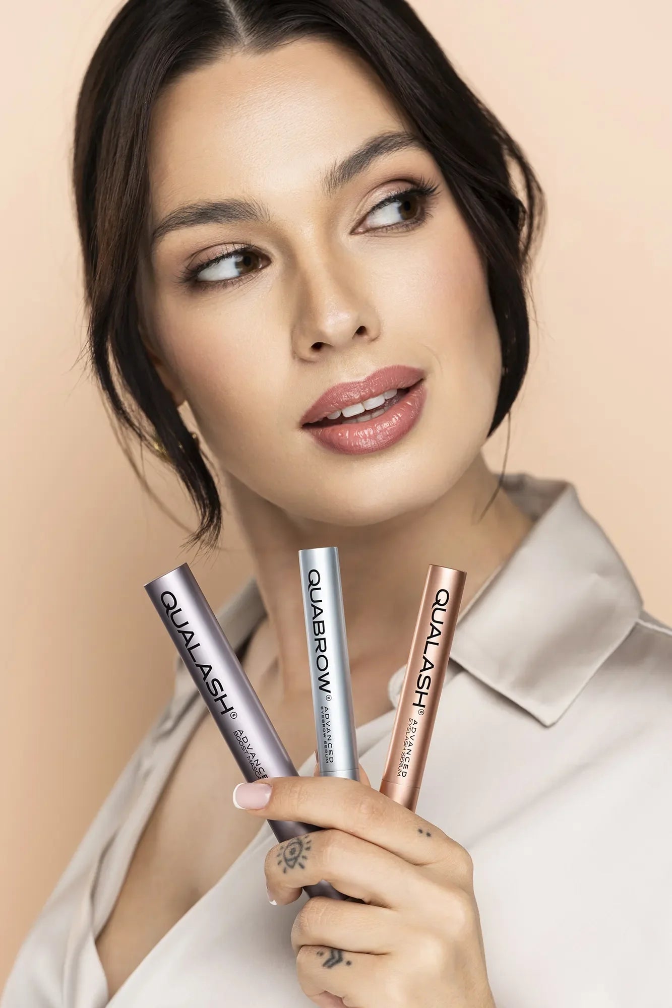 Woman holding three QUALASH & QUABROW products front-facing – lash and brow care