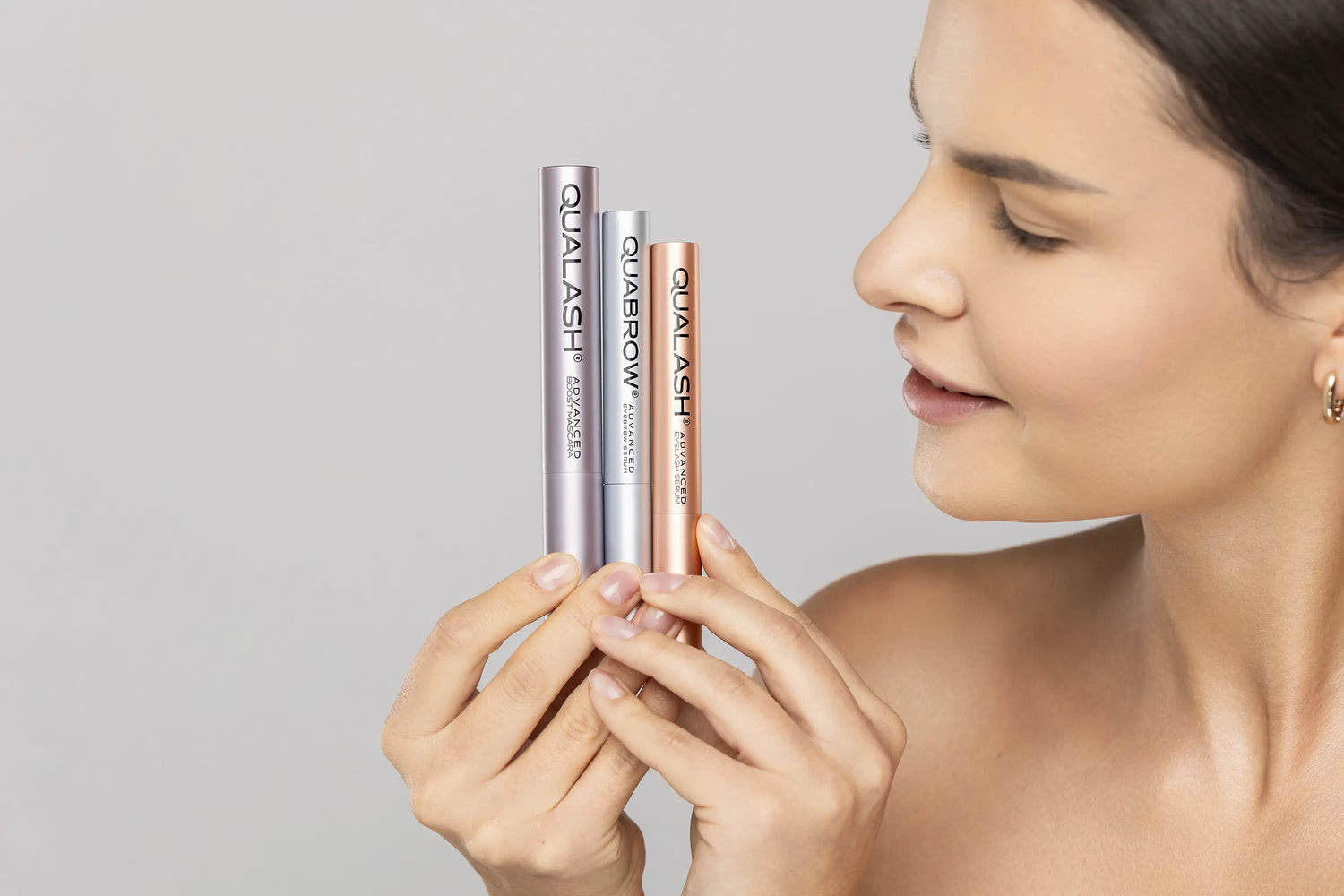 Woman holding QUALASH Boost Mascara, QUALASH Eyelash Serum, and QUABROW Eyebrow Serum – side view