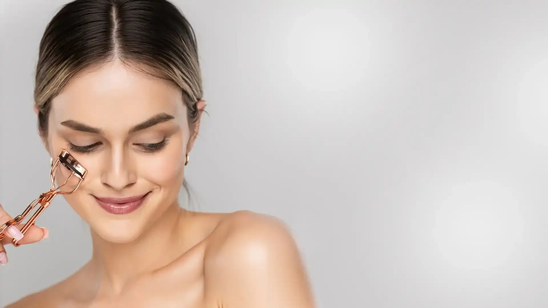 Woman using rose gold eyelash curler before applying Qualash serum