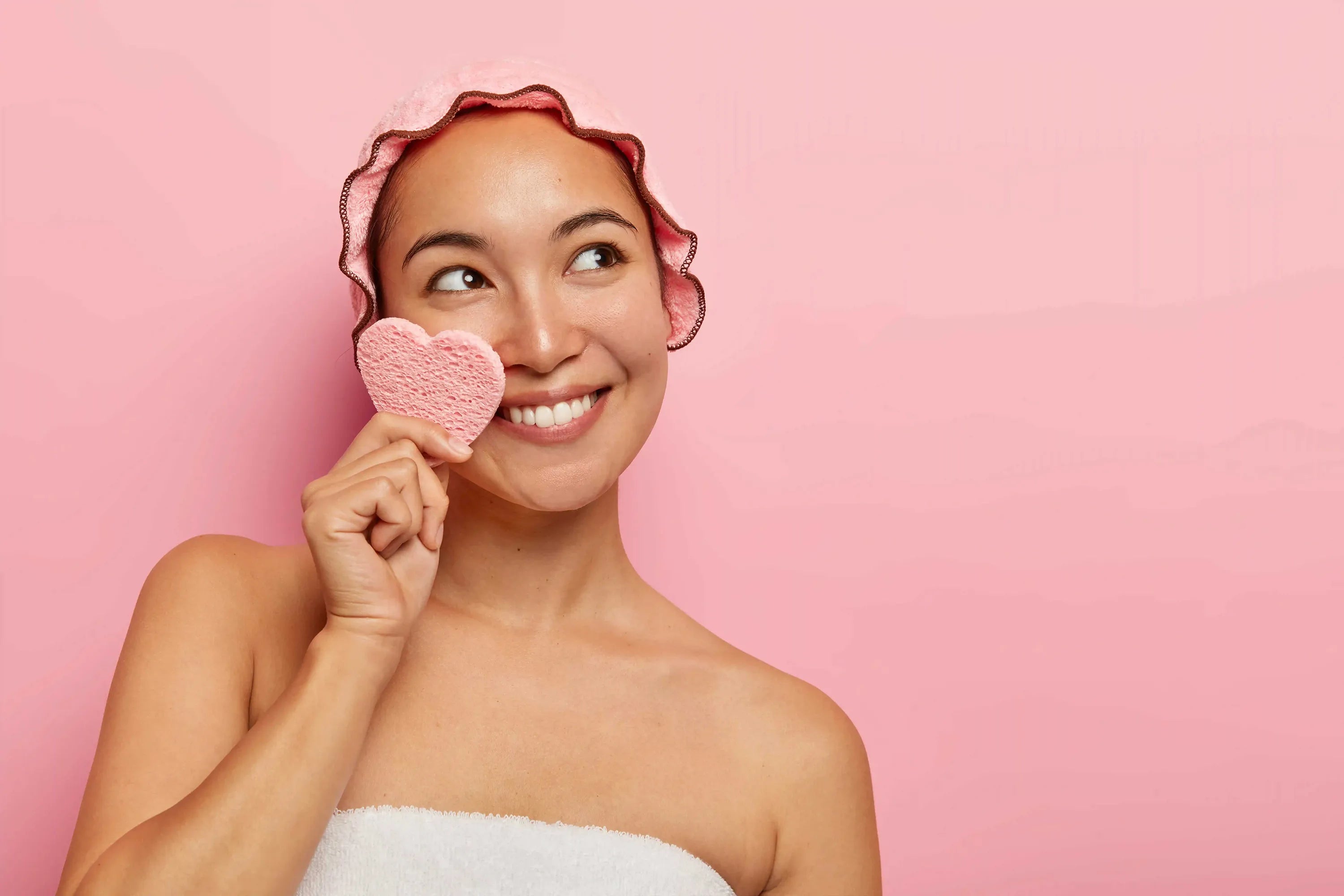 Femme heureuse tenant une éponge de nettoyage en forme de cœur pendant les soins du visage quotidiens